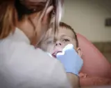 Chłopiec nie chce otworzyć ust u dentysty. Stomatolog próbuje go zbadać.