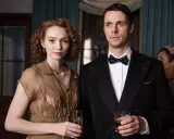 Ett elegant par med drinkar i handen, en scen från huset på udden serie. Kvinnan bär en brun klänning, mannen en smoking.