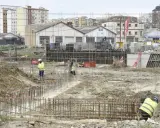 Obreros trabajan en la preparación de cimientos para nuevos proyectos de construcción. Se ven varillas de acero y maquinaria pesada en un día nublado.
