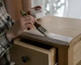 Persona pinta muebles de madera con brocha blanca.