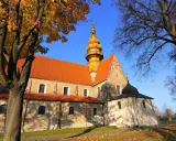 Kamienna świątynia z pomarańczowym dachem i żółtą wieżą, otoczona jesiennymi drzewami. To kościół św. Zbigniewa.