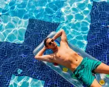 Uomo rilassato su un materassino in piscina, con gli occhiali da sole. Chissà se posso andare al mare se prendo l'antibiotico, pensa.