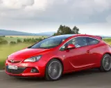 Czerwony Opel Astra J 1.4 Turbo z parą na pokładzie przemierza malowniczą trasę wśród zielonych pól i wzgórz.