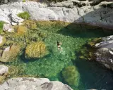 Una persona nada en unas cristalinas piscinas naturales Gredos, rodeadas de rocas y vegetación.