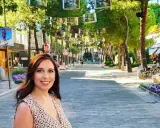 Donna sorridente in una strada alberata con negozi e fiori viola, un'atmosfera estiva nel centro di Milano Marittima.