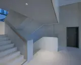 Moderne Treppe mit Sichtbeton-Wänden, die durch die Schalung eine interessante Textur erhalten. Ein dunkler Türrahmen und ein Holzhandschuh ergänzen das Bild.