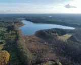 Malownicze jezioro Wolickie otoczone lasami i polami. Spokojna tafla wody odbija błękitne niebo z chmurami.