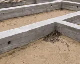 Betonowe fundamenty, czyli stan zero budynku, czekają na dalsze prace. Piasek i suche liście wypełniają przestrzeń.