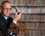 David Sedaris, con pipa in mano, seduto tra scaffali pieni di libri, riflette pensieroso.
