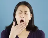 Une femme bâille, la main devant la bouche. Elle semble avoir besoin d'une pause pour réviser la conjugaison.