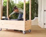 Une femme installe une bâche noire dans une jardinière en bois à roulettes, étape clé pour comment fabriquer toit pour tomates.