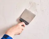Mano con espátula aplicando masilla para alisar paredes.