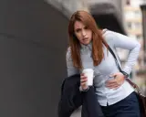 Kobieta z kubkiem kawy w dłoni odczuwa silne skurcze po alkoholu, trzymając się za brzuch.