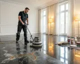 Mann mit Poliermaschine entfernt eingezogene Flecken aus Granit. Reinigungsmittel und Zubehör liegen bereit.