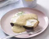 En bit stekt fisk med en krämig beurre blanc-sås och dill på en ljusrosa tallrik.