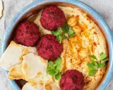 Rote Bete Falafel auf cremigem Hummus, garniert mit Kichererbsen und frischen Kräutern, serviert mit Pitabrot.