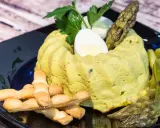 Delizioso flan di asparagi, guarnito con uovo sodo, asparagi freschi e grissini croccanti su un piatto nero.