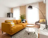 Sofá mostaza con cojines geométricos, mesa auxiliar redonda y alfombra gris. Los colores que combinan con el mostaza resaltan en esta sala.