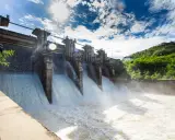 Ein Damm mit mehreren offenen Schleusen, aus denen kräftig Wasser strömt. Ein Beispiel für erneuerbare Energien durch Wasserkraft.