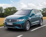 Un Volkswagen Tiguan R-Line verde oscuro se desplaza por una carretera rural, con campos dorados y árboles borrosos al fondo.