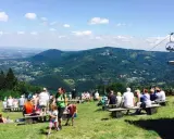 Widok na góry i miasto, ludzie odpoczywają na ławkach, w tle kolejka linowa. Bielsko-Biała atrakcje w pełnym słońcu.