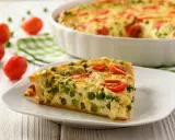Ein Stück vegetarische Quiche mit Erbsen und Tomaten auf einem Teller. Das ganze Gericht ist im Hintergrund zu sehen.