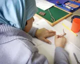 Kind mit Kopftuch schreibt im Heft. Trotz Opferfest und Schulfrei wird gelernt.