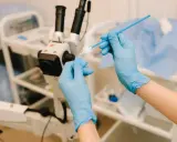 Ręce w niebieskich rękawiczkach przygotowują wymaz do badania gbs. W tle mikroskop i sprzęt medyczny.