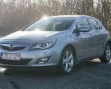 Szary Opel Astra z silnikiem 1.7 cdti zaparkowany na poboczu drogi, w tle drzewa i słońce.