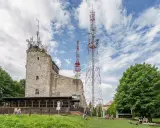 Kamienna wieża widokowa na Chełmcu, obok niej wysokie maszty telekomunikacyjne. Ludzie odpoczywają na trawie.