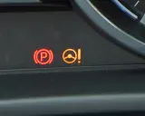 Kontrolka PS Nissan: czerwony symbol hamulca ręcznego i pomarańczowa kontrolka układu kierowniczego z wykrzyknikiem.