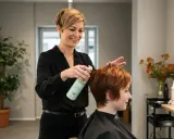Friseurin sprüht veganes Produkt ins Haar einer Kundin. Ein moderner vegan friseur Salon.