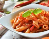 Eine Schüssel Penne Arrabiata, garniert mit Basilikum, mit scharfen Chilis und Knoblauch im Hintergrund.