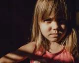 Niña con expresión seria, con luz de ventana en su rostro. A veces, mi hijo de 9 años se enoja por todo, pero hoy solo mira con intensidad.
