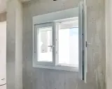 Instalar ventana PVC en obra gris. Ventana blanca de doble cristal con manilla plateada, lista para ser fijada.