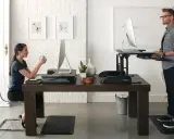 Un homme et une femme travaillent sur des bureaux réglables en hauteur. Une pause obligatoire pour le travail debout est essentielle pour leur bien-être.