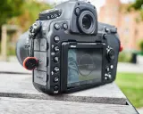 Nikon D850 test w plenerze. Aparat leży na drewnianym stole, w tle zieleń i budynek.