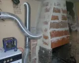 Instalación de tubo flexible para aprovechar calor de chimenea. Se ve una estufa azul y una chimenea de ladrillo.