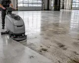 Profesjonalne czyszczenie posadzki betonowej za pomocą maszyny szorującej. Widać wyraźną różnicę między umytą a brudną powierzchnią.