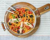 Pyszne spaghetti alla puttanesca z tuńczykiem, pomidorkami i czarnymi oliwkami w metalowej patelni, gotowe do podania.