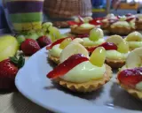 Pyszne babeczki z budyniem, udekorowane truskawkami, bananami i winogronami, wyglądają apetycznie.