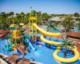Un parque acuático con toboganes amarillos y azules, palmeras y gente disfrutando. ¡Un lugar ideal para camping con toboganes en España!
