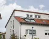 Ein Haus mit roten Ziegeln und Dachfenstern. Das Dach ist ein Pultdach, das nach einer Seite abfällt.