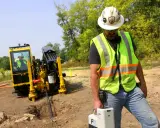 Trabajador supervisa una perforación horizontal dirigida con equipo especializado en un sitio de construcción.