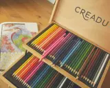 Miękkie kredki artysty malarza w drewnianej kasecie, obok kolorowanki z ptakiem.