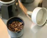 Kaffeebohnen in einer Schale neben einer Bialetti-Kaffeemaschine. Die Frage "bialetti wie viel kaffee" wird durch die Zubereitung beantwortet.