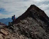 Alpinista na grani, zdobywający najwyższy szczyt Gruzji. W tle skaliste pasmo górskie i błękitne niebo.