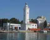 Il faro di Rimini, con la sua torre bianca e il porto con barche a vela, si staglia contro il cielo azzurro.