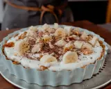Tarte banane caramel onctueuse, garnie de rondelles de banane, noix et copeaux de chocolat. Un délice gourmand.