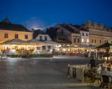 Wieczorny rynek w Kazimierzu Dolnym tętni życiem. Ludzie siedzą przy stolikach pod parasolami, ciesząc się atmosferą.